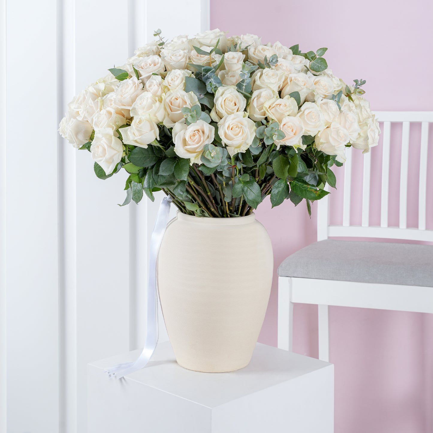 100 white roses in vase by Bloom Marbella arranged with greenery in a cream ceramic vase on white pedestal