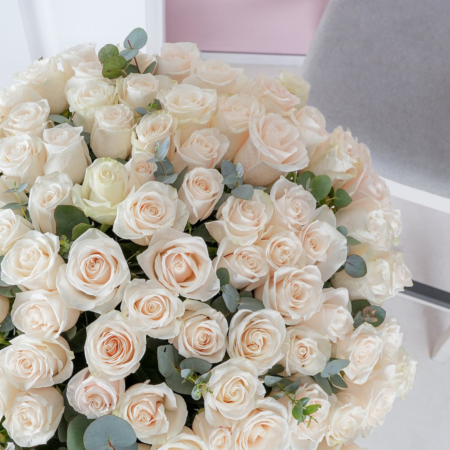 Bloom Marbella 200 white roses in vase with lush green foliage on a modern white table