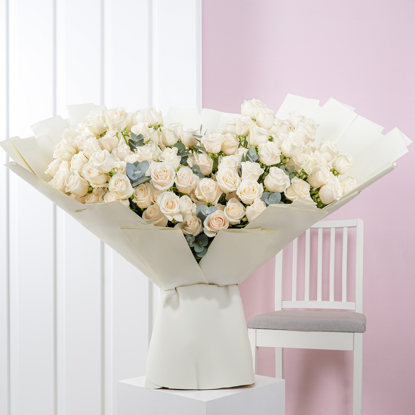 100 white roses bouquet Bloom Marbella wrapped in elegant white paper displayed indoors with a chair in background