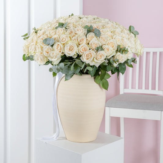 Elegant arrangement of 200 white roses in vase with green leaves by Bloom Marbella on white pedestal