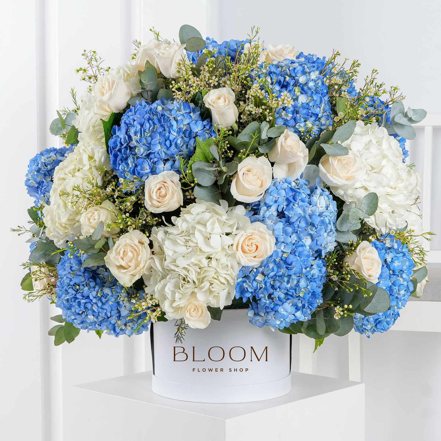 Blue hydrangea flower arrangement with white roses and greenery in a white Bloom Marbella vase