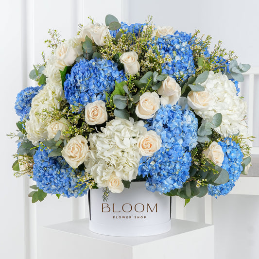Blue hydrangea flower arrangement with white roses and greenery in a white Bloom Marbella vase