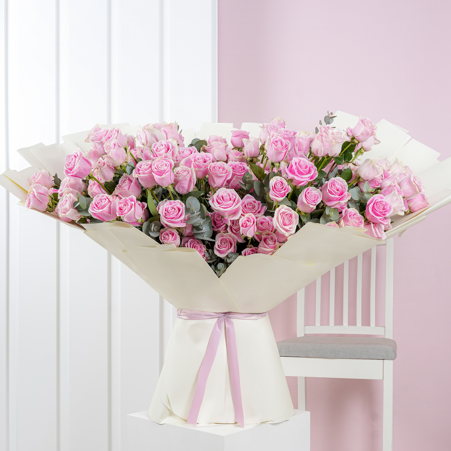 100 pink roses bouquet Bloom Marbella wrapped in white paper with pink ribbon displayed on white pedestal