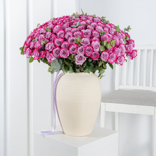 100 purple roses in vase - Bloom Marbella, Spain arranged in cream vase with green leaves on white pedestal