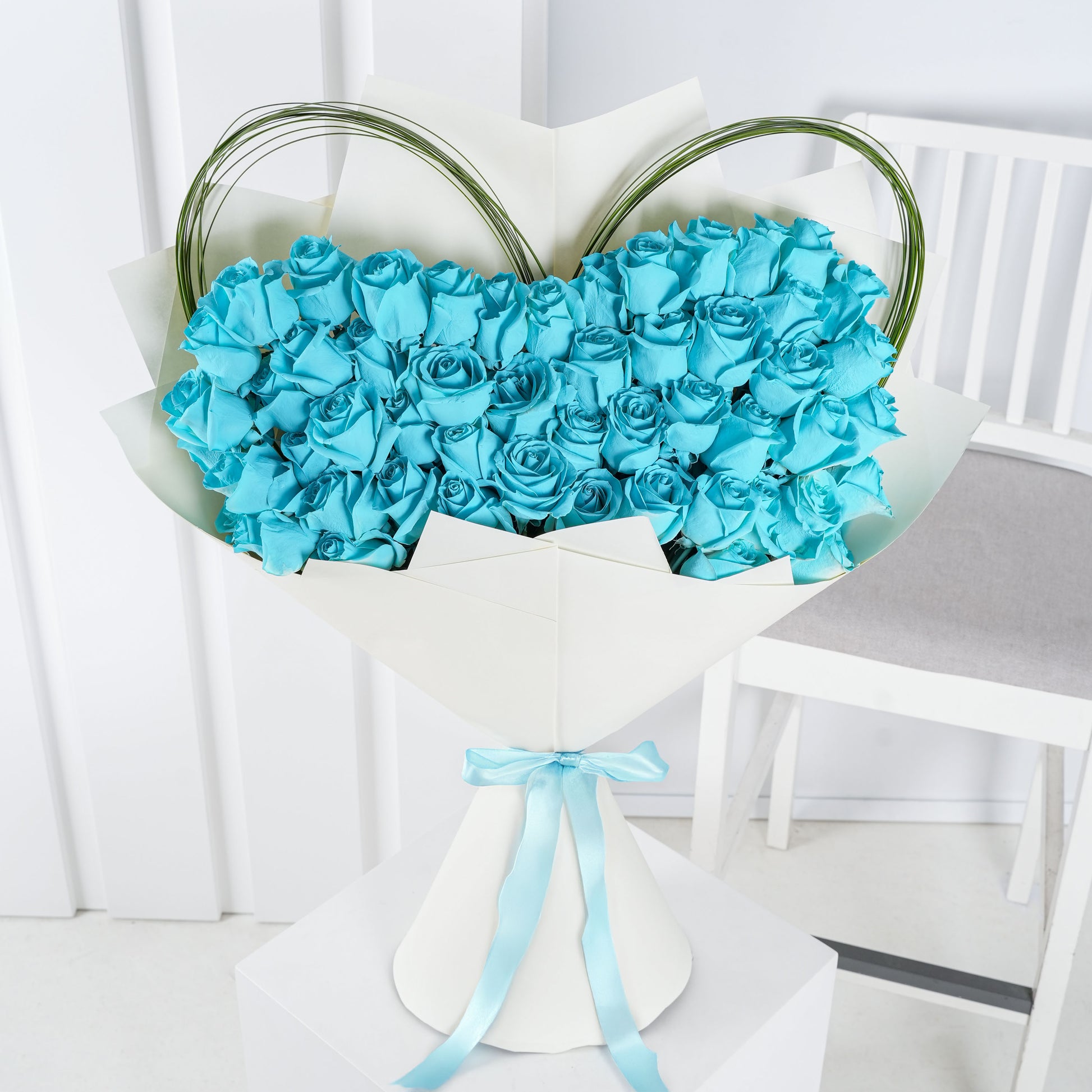 Elegant blue rose bouquet Marbella with heart-shaped design wrapped in white paper and tied with blue ribbon