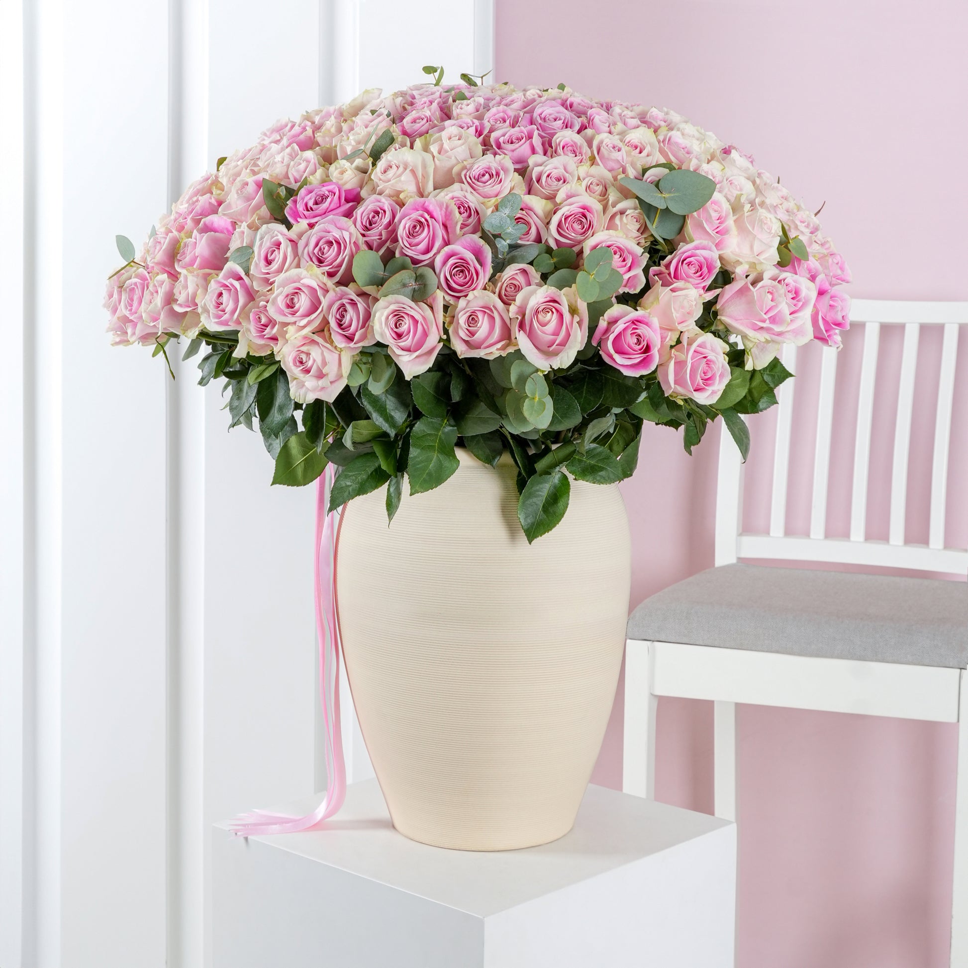 Large bouquet of pink roses in a cream vase displayed next to a white chair pink roses vase Marbella