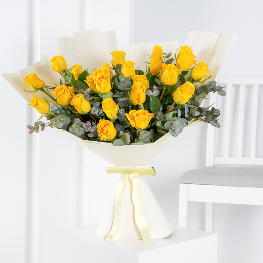 Bright yellow rose bouquet Marbella wrapped in cream paper with green foliage and yellow ribbon